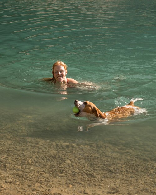 Милая собака держит мяч и плавает рядом со своим владельцем