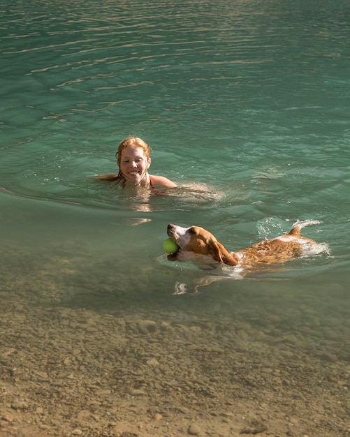 Cute dog holding a ball and swimming next to his owner