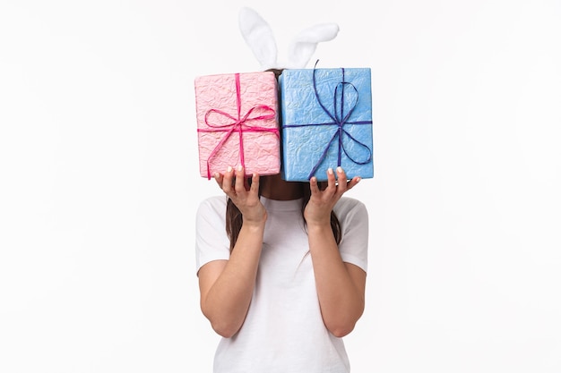 Free photo cute easter bunny female in rabbit ears, hiding her face behind pastel wrapped gift boxes