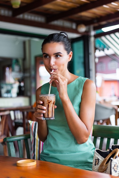 Foto gratuita la donna felice calma elegante sveglia in vestito verde da estate si siede con il caffè nella caffetteria godendo la mattina