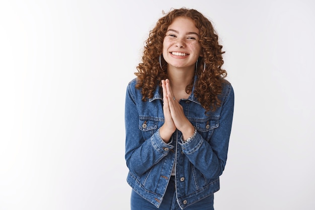 Cute energized friendly-looking charming redhead freckles girl wearing denim press palms together make angel smile gaze begging favor hand pray, say please lending money, standing white background