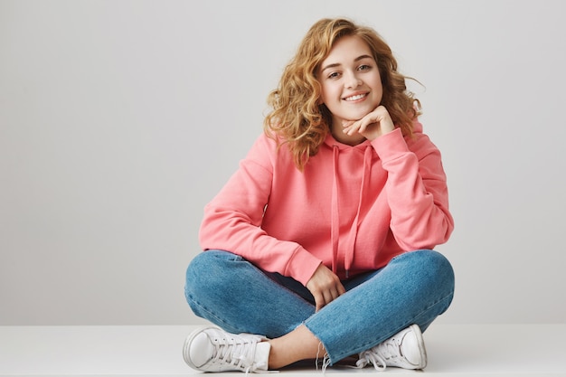 Cute excited girl student sitting on floor with crossed feet