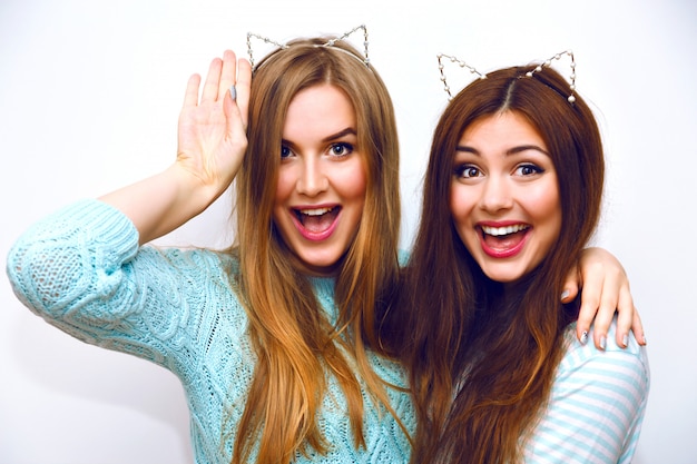 Cute fashion portrait of pretty sisters women having fun together hugs and going crazy, funny cat ears, mint winter sweaters, white wall, best friends, joy, trend, relations, happy, natural make up.