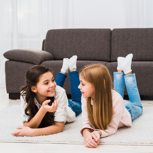 Cute female friends lying on carpet talking to each other