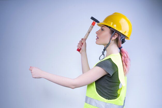 Cute female worker trying to hammer a nail into the wall