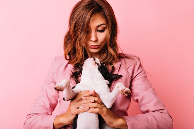 生姜の女性を見上げているかわいいフレンチブルドッグ。彼女の子犬を保持している熱狂的な巻き毛の女性の屋内ショット。