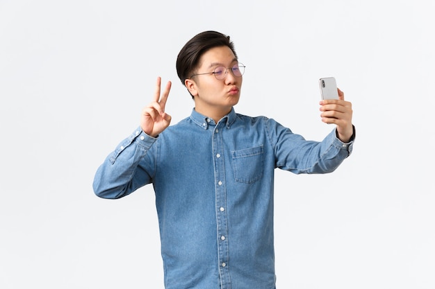 Free Photo | Cute and funny asian young guy pouting silly, taking selfie on smartphone, using photo filter app to change appearance, shooting himself with peace sign and kiss, white background. Free Photo | Cute and funny asian young guy pouting silly, taking selfie on smartphone, using photo filter app to change appearance, shooting himself with peace sign and kiss, white background.