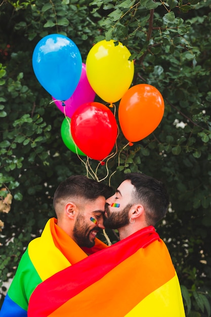 Cute gay sweethearts embracing wrapped in rainbow flag