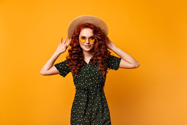 Cute ginger girl touching straw hat with smile. Front view of amazing european woman posing on yellow background.