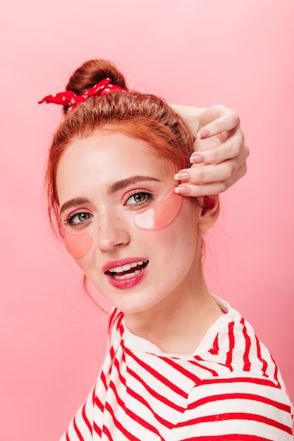 Cute ginger girl with eye patches looking at camera. stunning young woman posing with gently smile on pink background.