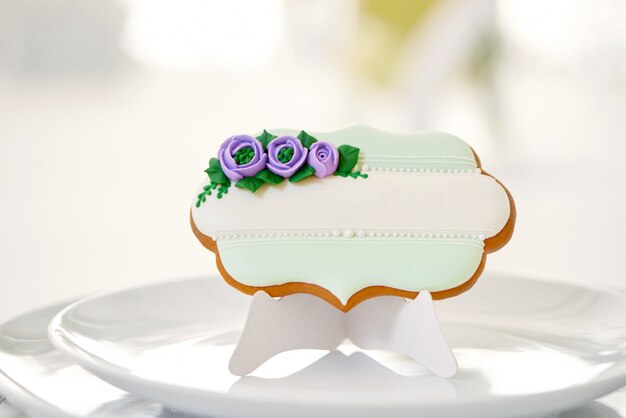 Симпатичные имбирные пряники, засахаренные синей и зеленой глазурью и жемчугом, стоит на белой тарелке на столике в ресторане, накрытой белоснежной скатертью. Прекрасное украшение для праздничного стола.