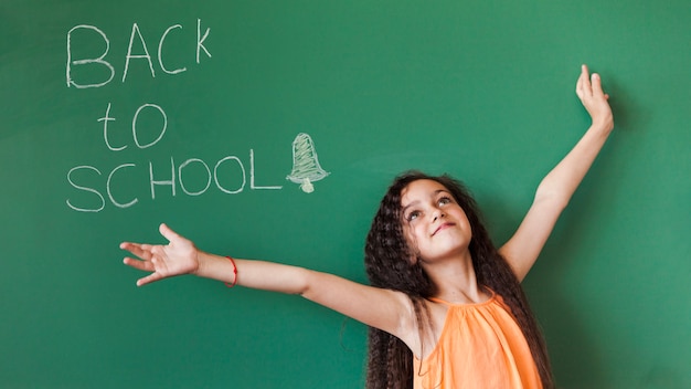 Free photo cute girl at blackboard with hands apart