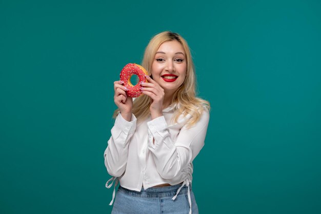 Cute girl blonde beautiful young girl in a white neat shirt excited holding pink donut