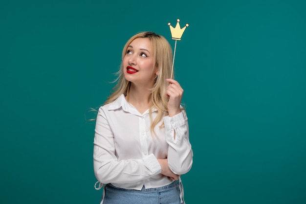 Ragazza carina bionda bella ragazza in una camicia bianca ordinata che osserva in su pensando con la corona falsa