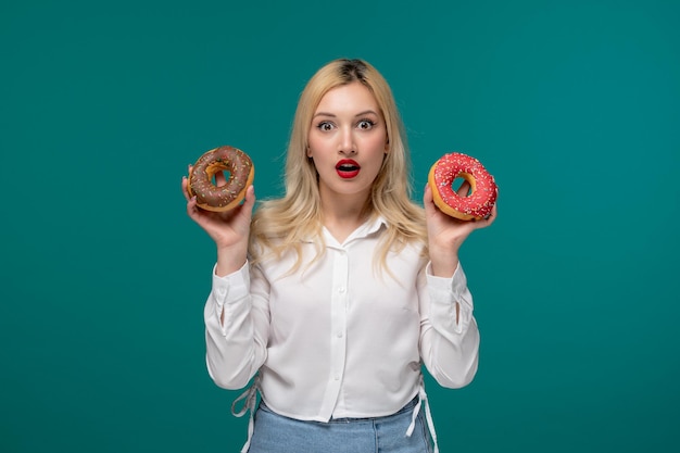 Cute girl blonde beautiful young girl in a white neat shirt shocked with donuts