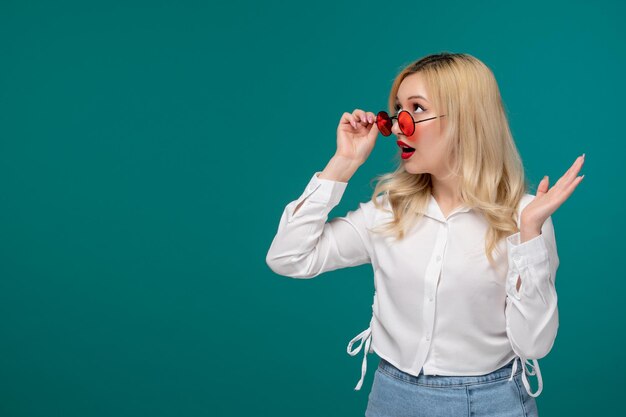 Cute girl blonde young pretty girl in a white shirt overlooking sunglasses and waving hands