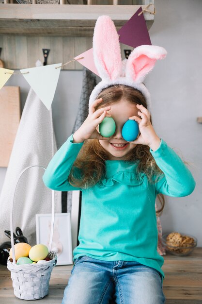 Милая девушка в ушах зайчика держит крашеные яйца на глазах