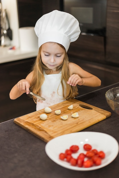 Cute girl cutting egg slices on chopping board with knife