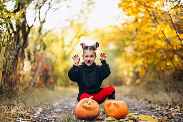 Free photo cute girl dressed in halloween costume outdoors with pumpkins