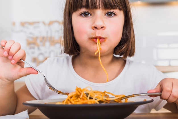 Cute girl eating delicious pasta in kitchen