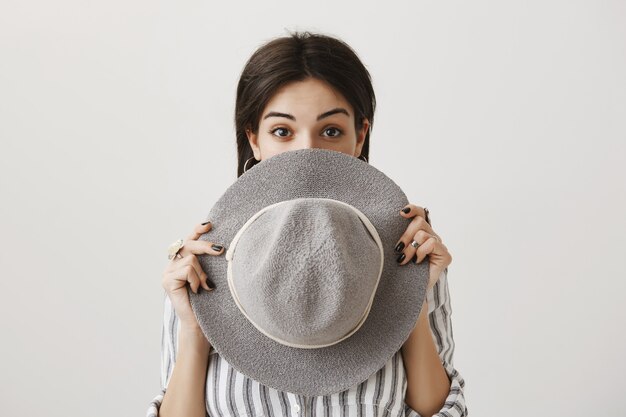 Cute girl hiding face behind stylish hat