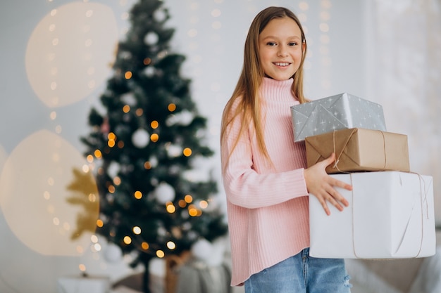 Cute girl holding christmas presents by christmas tree