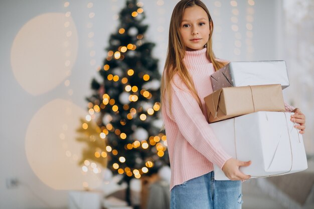 Cute girl holding christmas presents by christmas tree