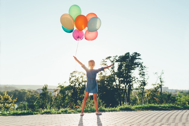 Cute girl holding colorful balloons in the city park