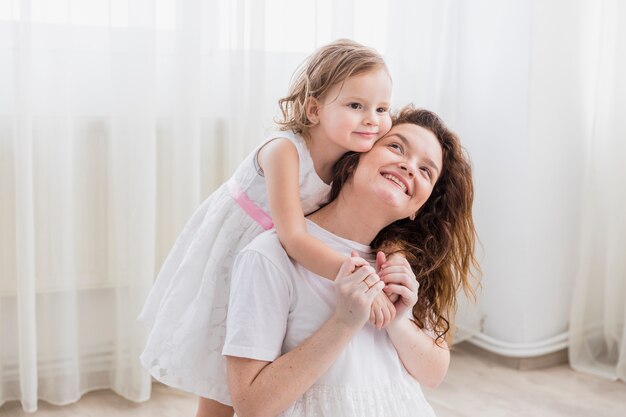 Cute girl hugging her happy mother from the back at home