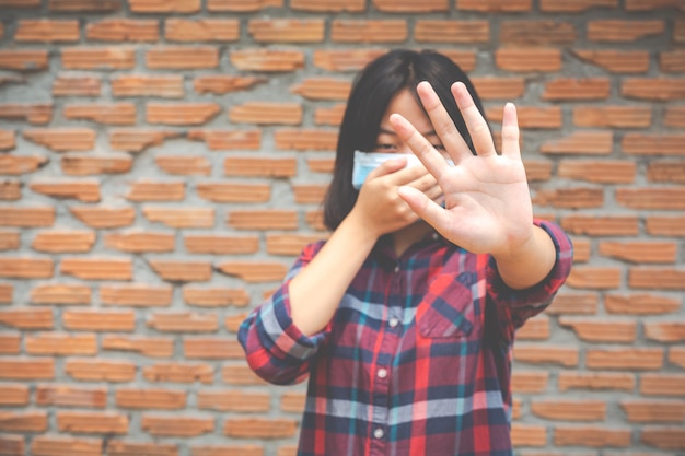 Foto gratuita la ragazza sveglia sta indossando la maschera e sta facendo la mano di arresto dall'altra parete della parete del rick del prople onb