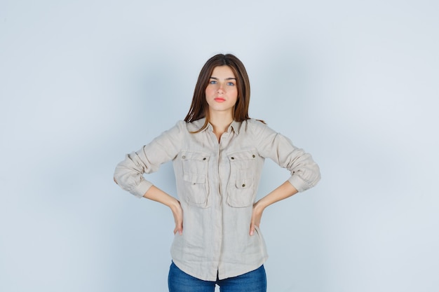 Cute girl keeping hands on waist in shirt and looking concerned.