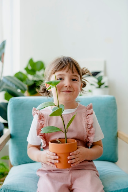 家で鉢植えの植物を保持しているかわいい女の子の子供