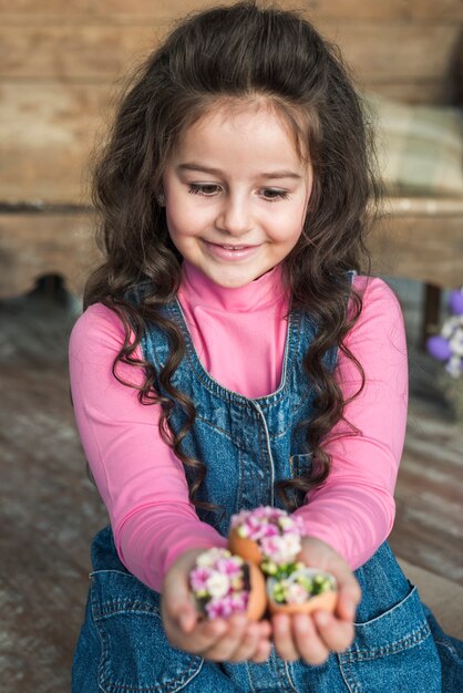 Cute girl looking at broken eggs with flowers 