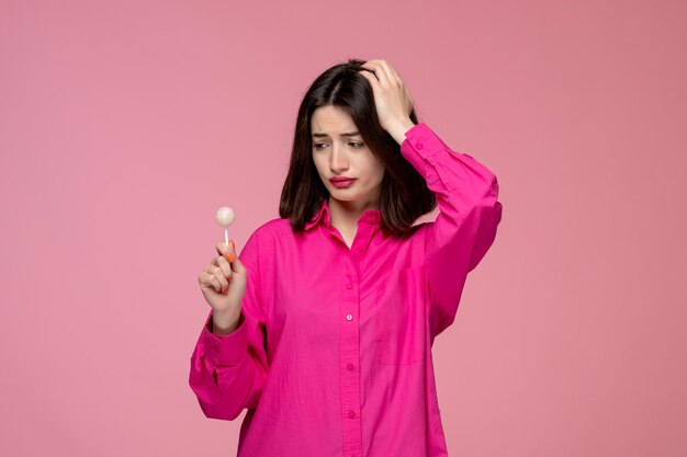 Cute girl lovely young brunette girl in pink shirt with red lipstick looking at white lollipop