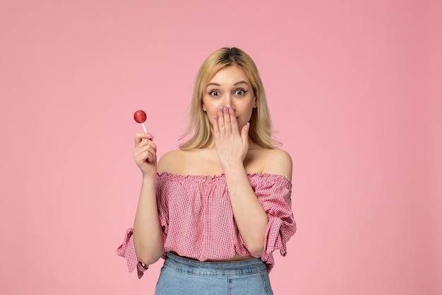 Ragazza carina ragazza adorabile con rossetto rosso in camicetta rosa scioccata in possesso di una caramella dolce rotonda