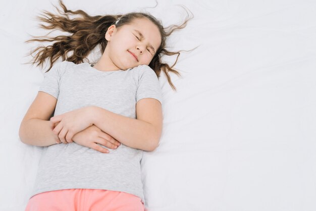 Cute girl lying on white bed suffering from stomach ache