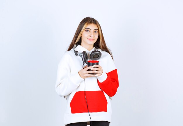 A cute girl model standing in headphones and holding a cup of drink