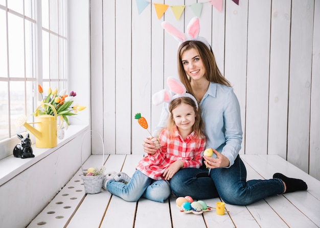 Foto gratuita ragazza carina e madre nelle orecchie di coniglio seduto con le uova di pasqua