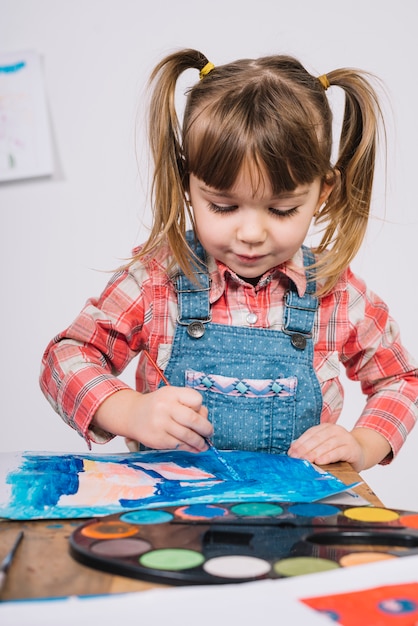 Cute girl painting with blue gouache at wooden table