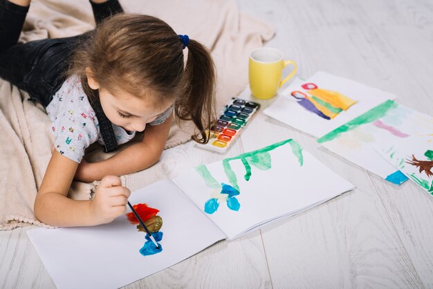 Cute girl painting with bright aquarelle on floor