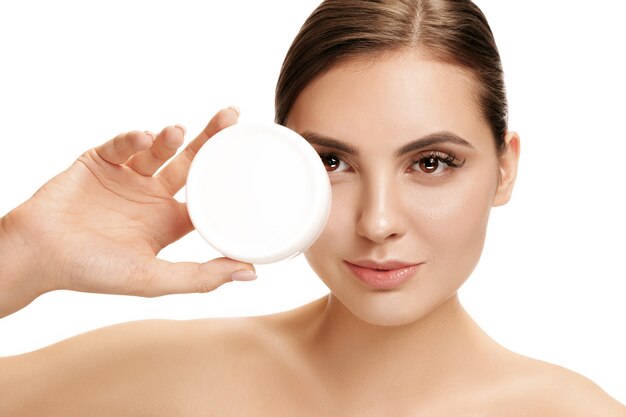 Free photo cute girl preparing to start her day. she is applying moisturizer cream on face at studio. the beauty, care, skin, treatment, health, spa, cosmetic and advertising concept