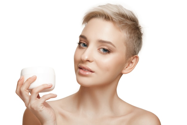 Cute girl preparing to start her day. She is applying moisturizer cream on face.