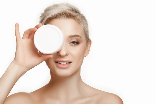 Cute girl preparing to start her day. She is applying moisturizer cream on face.