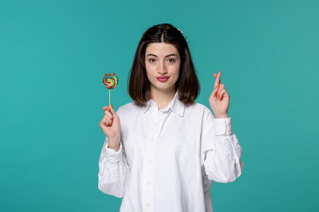 Cute girl pretty brunette young sweet girl in white shirt crossing fingers with lollipop