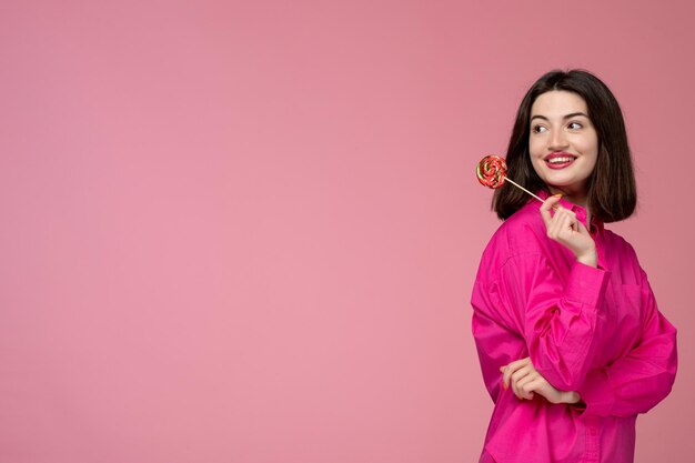 Cute girl pretty young beautiful brunette girl in pink shirt looking behind with lollipop