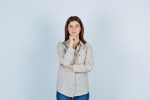 Cute girl propping chin on hand in shirt and looking pensive.