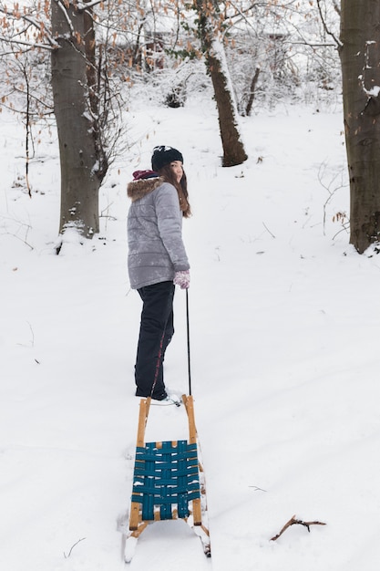 Cute girl pulling empty sledge on snowy landscape in winter