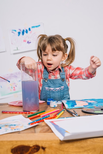 Cute girl putting paint brush into muddy water