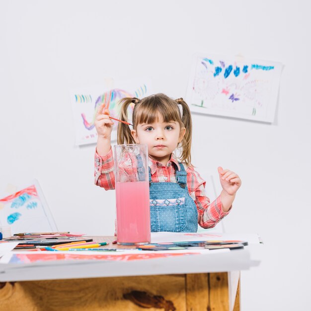 Cute girl putting paint brush into water glass