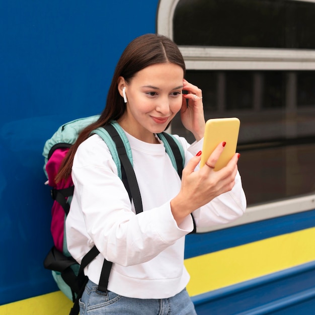 Cute girl at the railway station looking into mobile mirror